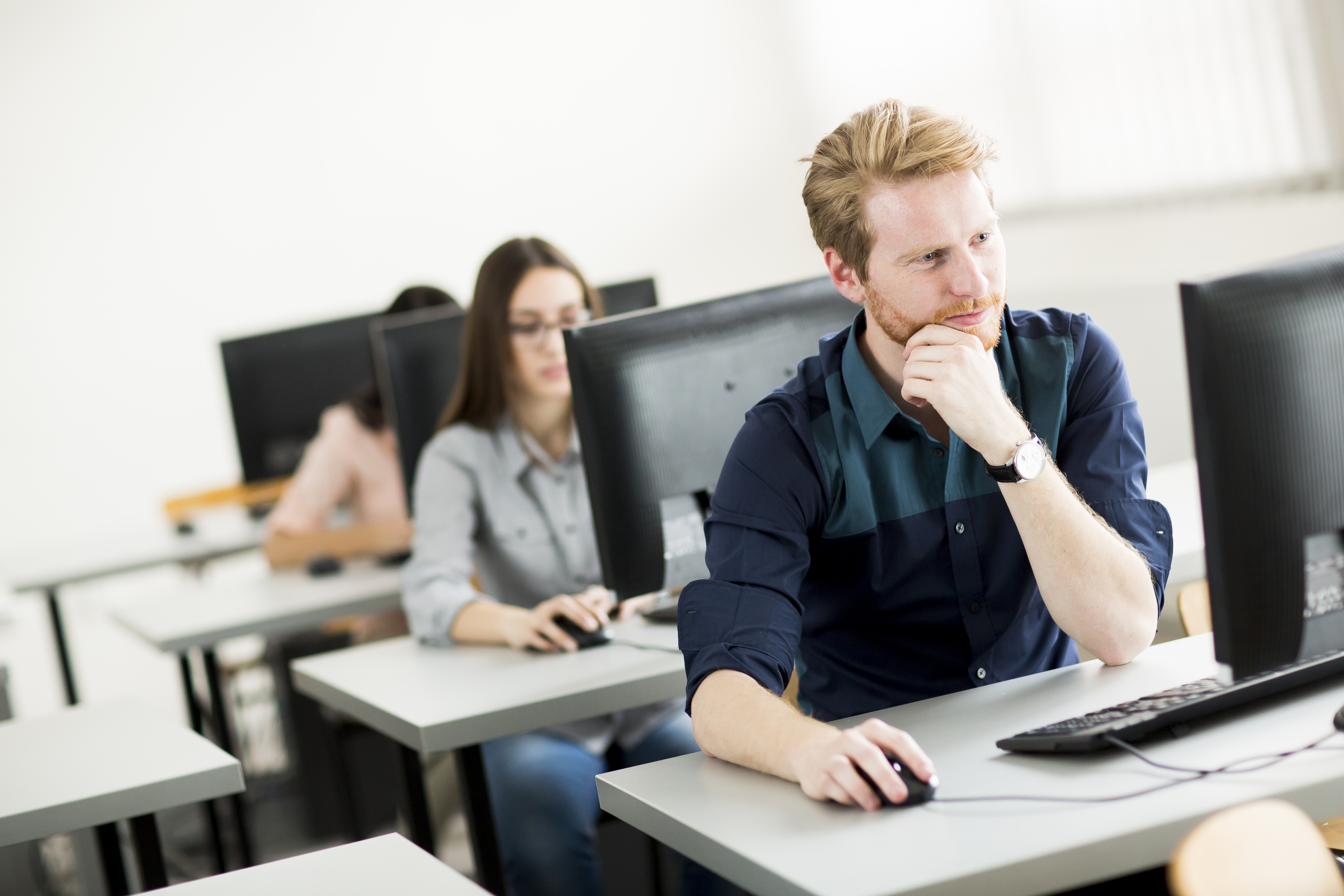 Man and woman sitting behind computers taking an exam