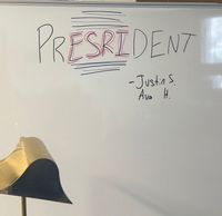 Img Description: White board with black letters saying "PRESRIDENT" with the names Justin S and Ava H below it.
